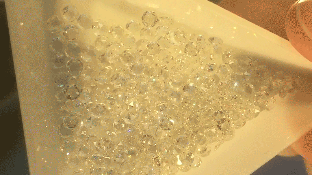 A white tray filled with diamonds. Light catches the edges of the gemstones as the tray moves back and forth, making them appear sharp and shard-like.