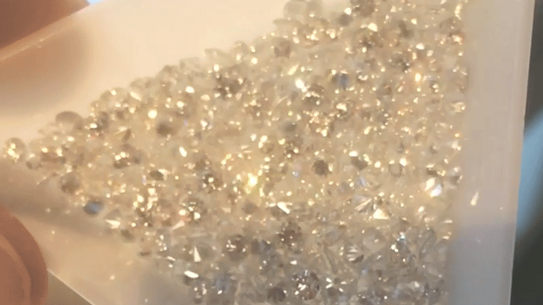 A white tray filled with diamonds. Light catches the edges of the gemstones as the tray moves back and forth, making them sparkle.