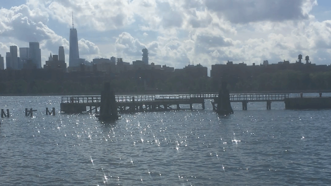 A river lit up in sparkles, a dock in the foreground and the skyline in the distance.