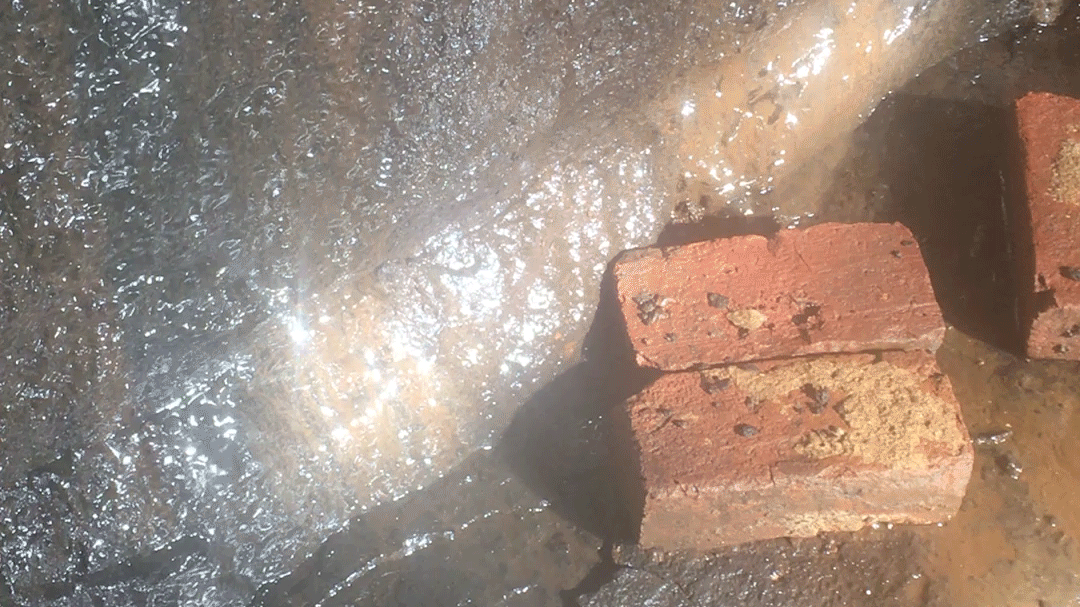 Water streaming down stone, a piece of light landing squarely on it. Two mud-covered bricks lay off to the side, at the stone’s base.