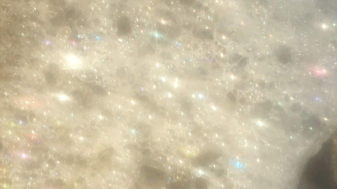 A close up of foam. Light plays across the bubbles big and small, producing a glittering effect. Airy but dazzling, threatening to disappear at any moment.