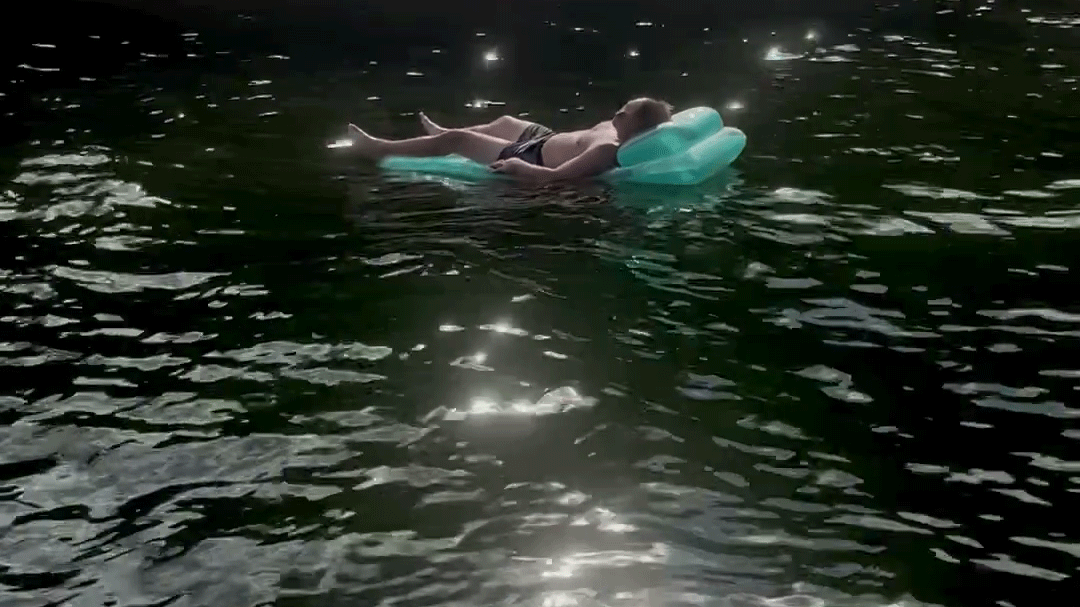 Luke floating on the lake in a fluoride green inflatable, surrounded by glimmering water.