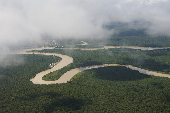 Wispy clouds hanging low over the meander of the Atrato River in the Andes, couched in a dense, flat forest.